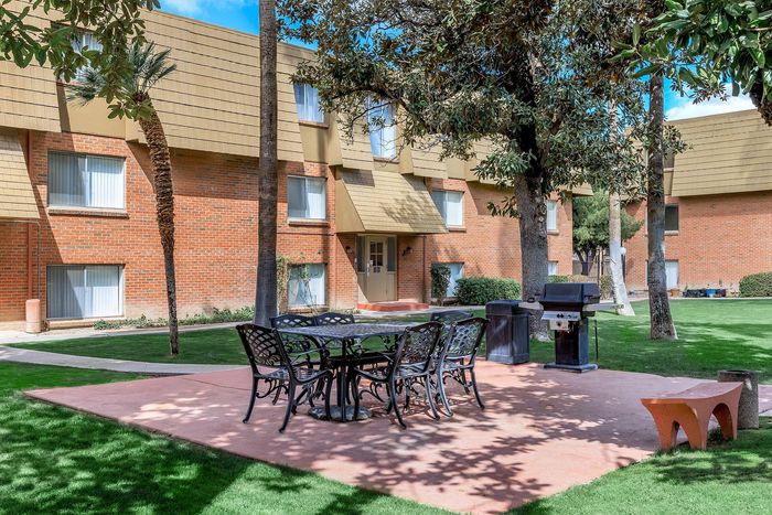 Charming apartment complex courtyard with modern outdoor seating, lush green grass, and a barbecue grill for sunny gatherings.