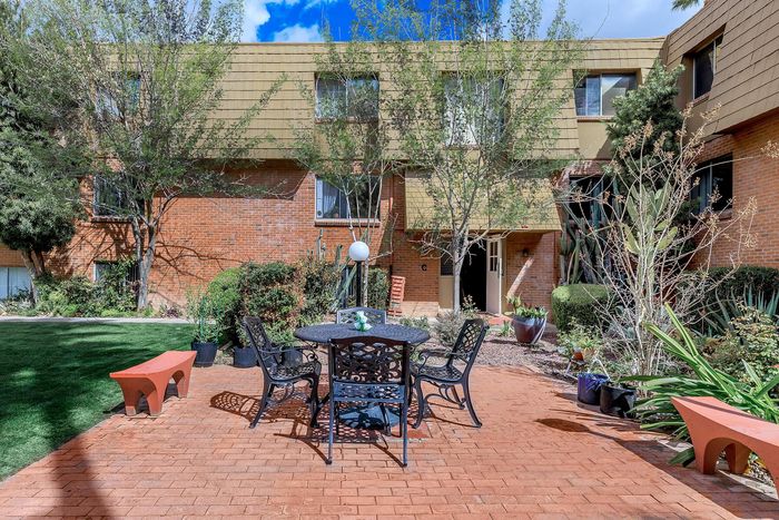 Charming courtyard with lush greenery, featuring a wrought iron table and chairs set on a red brick patio, perfect for outdoor relaxation.