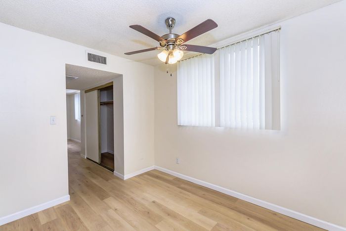 Bright and airy room with elegant hardwood floors, modern ceiling fan, and ample natural light through vertical blinds.