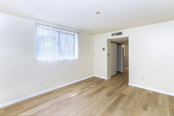 Bright and spacious room with elegant hardwood floors and a large window, perfect for creating a personalized living space.