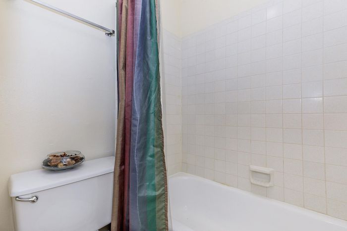 Bright and inviting bathroom featuring a tiled shower with a multi-colored curtain, offering a serene and stylish space.