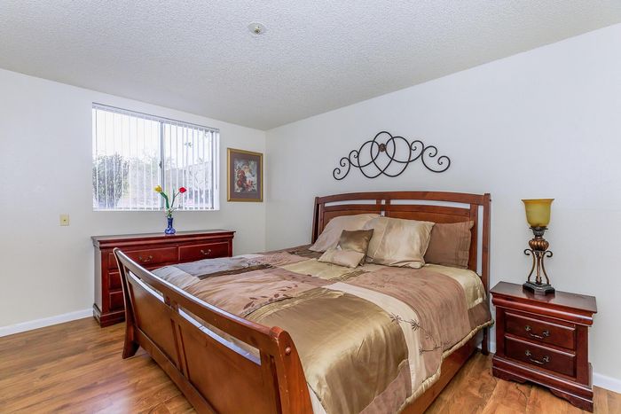 Elegant bedroom with a rich wooden bed frame, matching dresser and nightstand, and tasteful decor, illuminated by natural light from a large window.