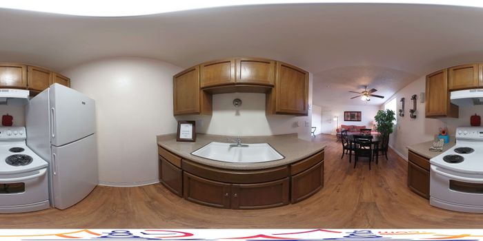 Inviting kitchen view with sleek countertops, ample wooden cabinetry, and a cozy adjacent dining area, elegantly lit with a modern ceiling fan.