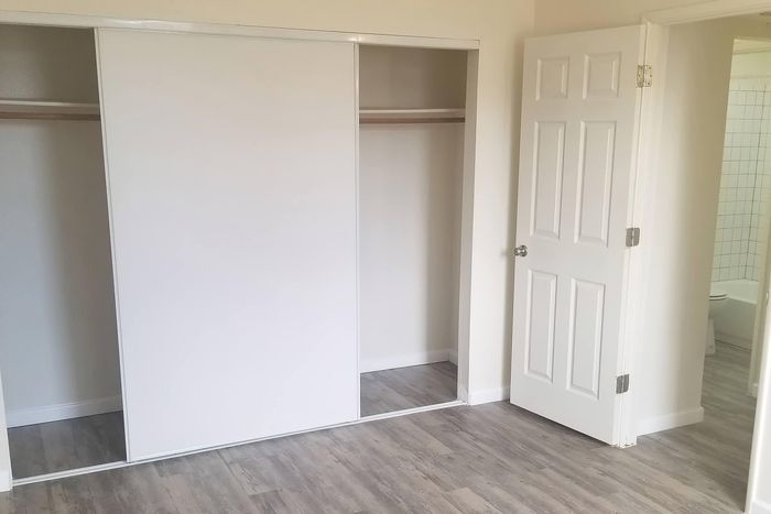 Bright and inviting room with sleek sliding closet doors and elegant wood flooring, offering access to a modern bathroom.