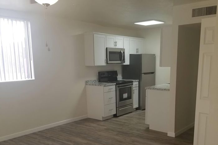 Modern kitchen with sleek stainless steel appliances, elegant white cabinetry, and stylish granite countertops, featuring warm wood flooring.