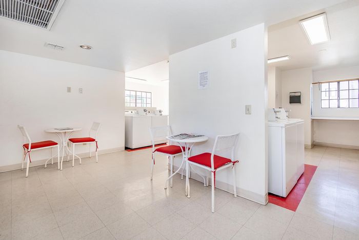 Bright apartment laundry room with sleek washers, chic tables with red-accent chairs, and natural light from large windows.