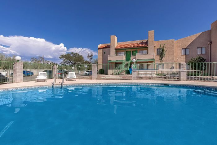 Charming apartment complex with a refreshing swimming pool, poolside loungers, and vibrant architecture under a clear blue sky.