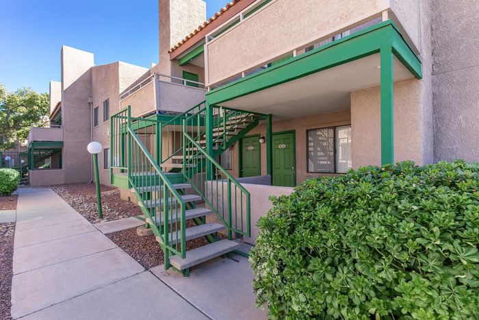 Inviting apartment exterior with charming green accents and lush landscaping on a sunny day.
