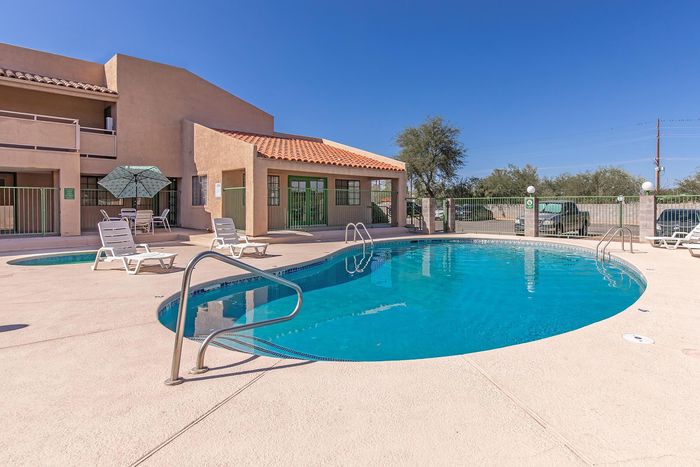 Inviting outdoor pool area at sunny apartment complex, featuring cozy lounge chairs and shaded patio seating.