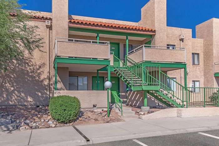 Charming apartment exterior with vibrant green accents, surrounded by landscaping and a clear blue sky, highlighting a welcoming entrance.