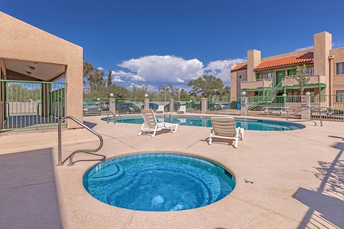 Inviting outdoor pool area with sun loungers, surrounded by vibrant greenery and charming architecture under a bright blue sky.