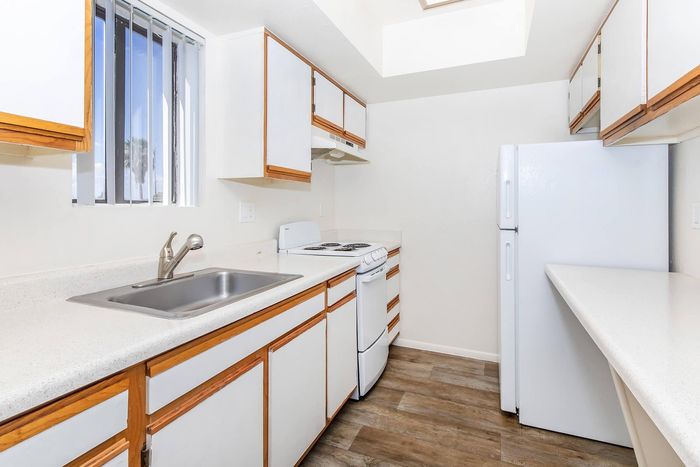 Bright, modern kitchen with sleek white cabinetry, laminate flooring, and ample counter space, perfect for culinary enthusiasts.