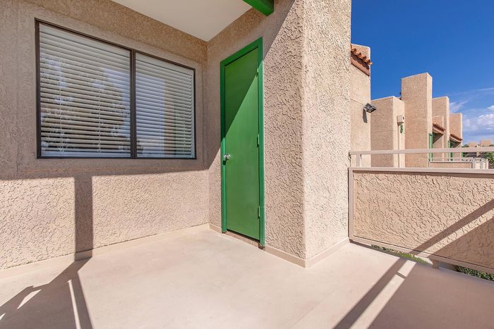 Charming balcony with textured walls, green door, and sunny sky views, perfect for relaxation.