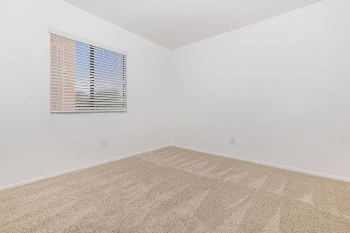Bright, cozy bedroom with fresh carpeting, large window with blinds, and minimalist white walls providing a blank canvas for personal design.