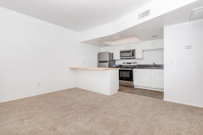 Modern open-concept kitchen with stainless steel appliances, elegant white cabinetry, and cozy carpeted living space.