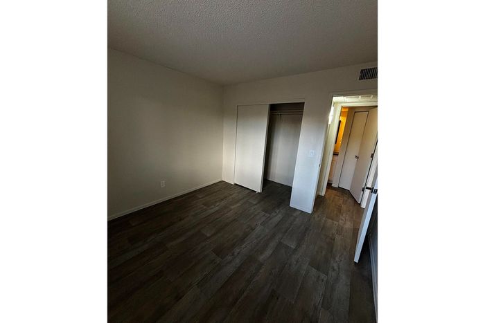 Spacious bedroom with elegant dark wood flooring, ample closet space, and bright natural light&mdash;a perfect canvas for personalized touches.