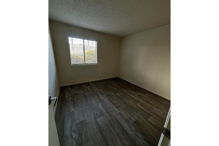 Inviting bedroom with warm natural light, featuring sleek hardwood flooring and soft, neutral walls.