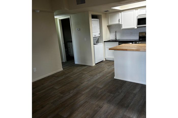 Modern apartment kitchen with sleek white cabinetry, hardwood floors, and a convenient in-unit washer and dryer.