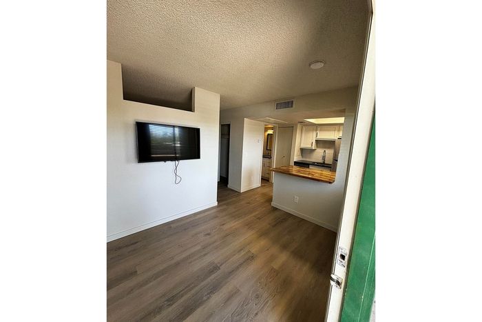 Inviting modern apartment interior featuring a mounted TV, sleek wooden floors, and a stylish open-concept kitchen with white cabinetry.