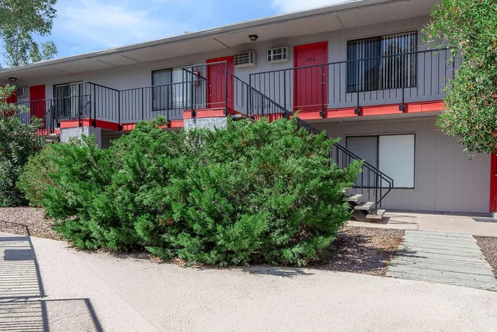Charming apartment exterior with vibrant red doors, inviting outdoor staircase, and lush greenery, offering a cozy living environment.