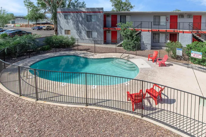 Inviting outdoor pool area with vibrant red lounge chairs, surrounded by greenery and modern apartment architecture.