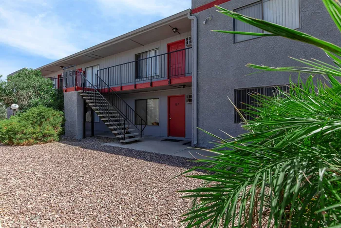 Charming apartment exterior with vibrant red doors and lush greenery, featuring modern balcony design and a serene stone courtyard.