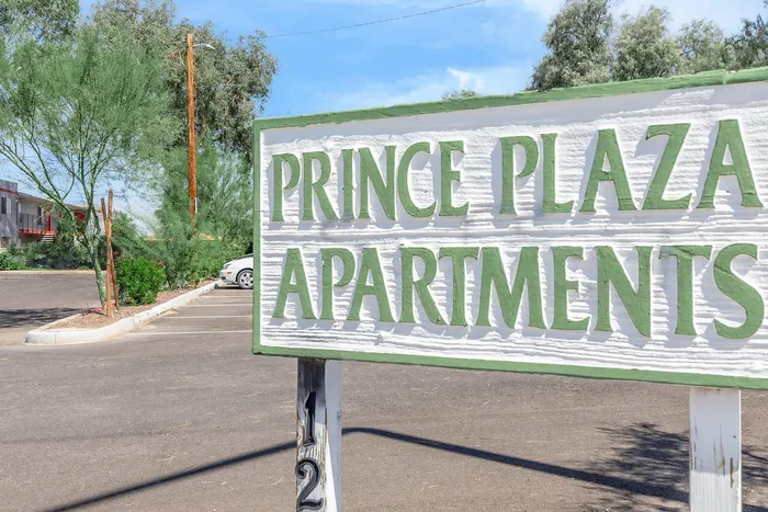 Charming entry sign for Prince Plaza Apartments, set amidst lush greenery and a spacious parking area.