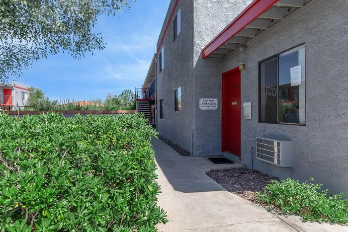 Inviting apartment exterior showcasing a vibrant red door and lush greenery in a serene setting.