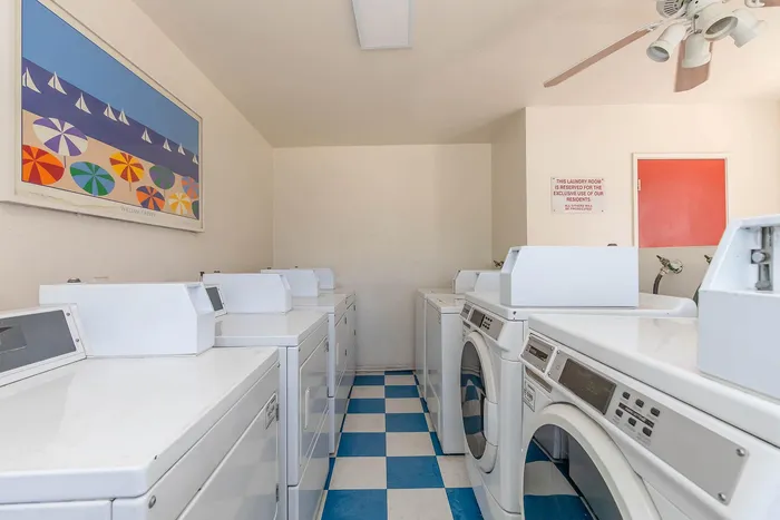 Bright and airy laundry room with modern washing machines, vibrant artwork, and checkerboard flooring, perfect for residents.