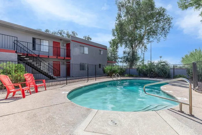 Bright apartment complex with inviting pool and vibrant red chairs set against a clear blue sky, offering a refreshing outdoor escape.
