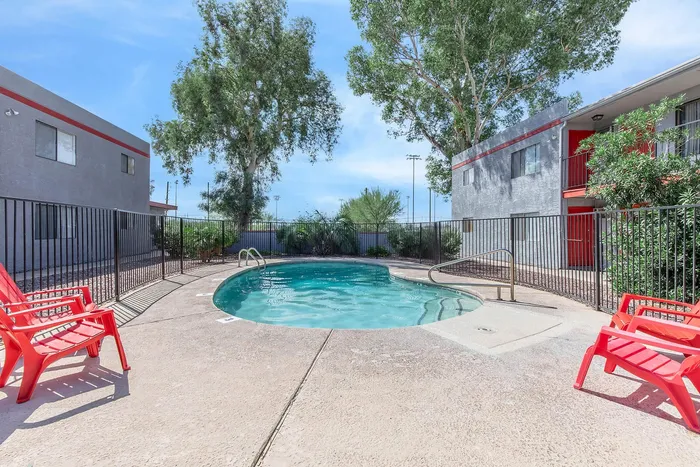 Inviting outdoor pool area with vibrant red chairs, surrounded by lush greenery and modern apartments.