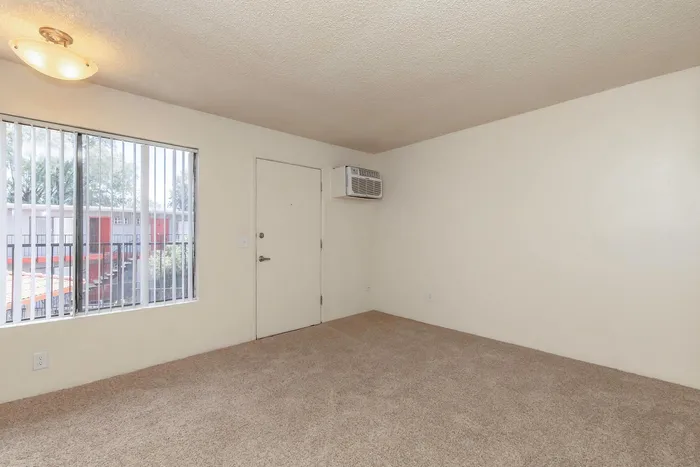 Bright and inviting corner room with plush carpeting, large window for natural light, and modern wall AC unit.