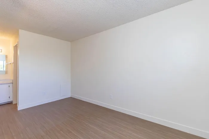 Bright room with sleek hardwood flooring, minimalist design, and a vanity leading to a bathroom.
