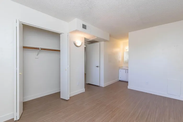 Bright and airy bedroom with sleek wood flooring, open closet space, and access to an adjacent bathroom, perfect for modern living.