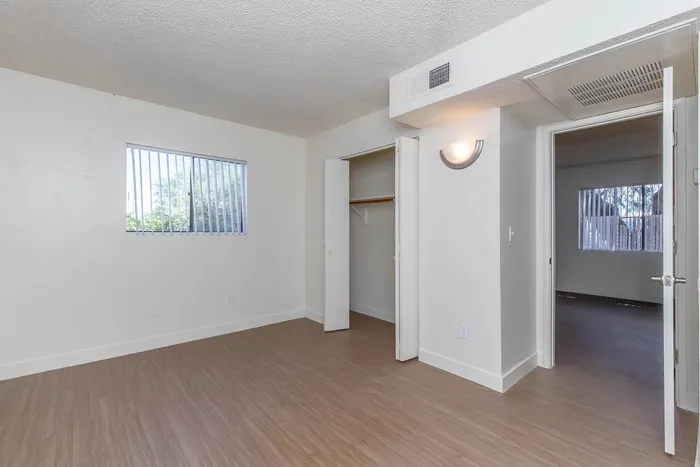 Bright and inviting bedroom with large window, natural light, and sleek wooden floors, perfect for modern living.