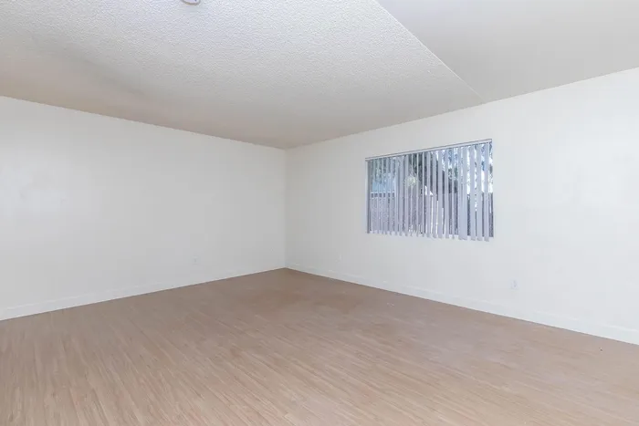Bright and spacious living area with modern wooden flooring, large window with vertical blinds providing ample natural light.