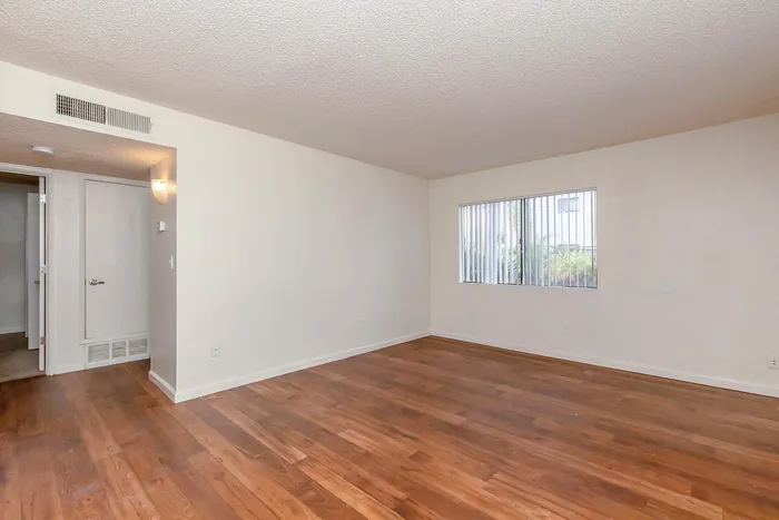Inviting apartment interior with warm wood flooring, neutral walls, and abundant natural light through a large window.