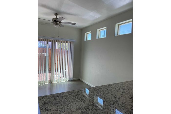 Bright living space with modern ceiling fan, natural light from high windows, and sliding glass door opening to a private fenced yard.