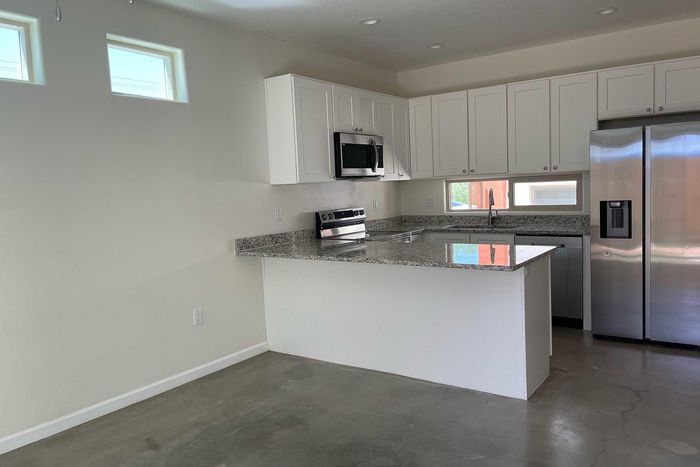 Modern kitchen featuring sleek granite countertops, bright white cabinetry, and stainless steel appliances in a spacious, airy layout.