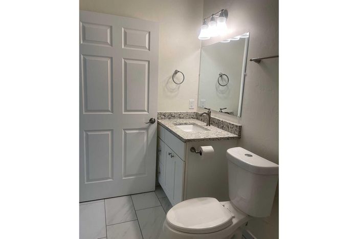 Elegant bathroom with granite countertop, modern fixtures, and sleek tile flooring, featuring ample lighting and stylish cabinetry.