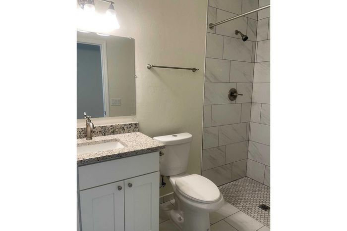 Modern bathroom with elegant granite countertop, sleek white cabinetry, and a stylish walk-in shower.
