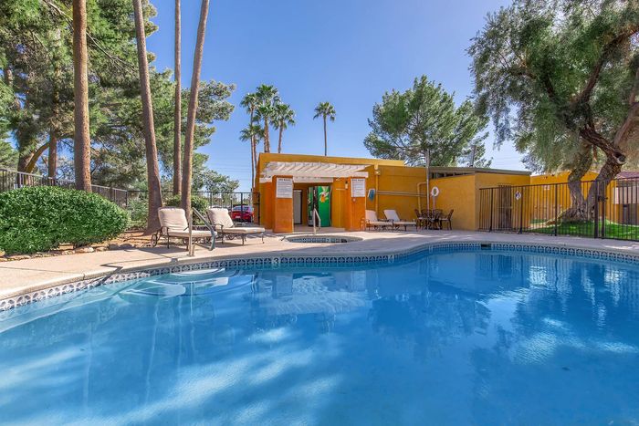Inviting outdoor pool area with lush greenery, lounge chairs under a pergola, and a vibrant clubhouse, perfect for relaxation and entertaining.