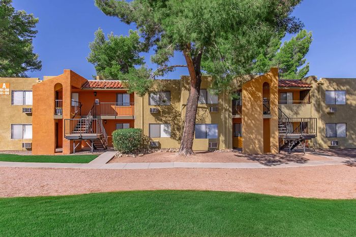Charming apartment complex featuring vibrant architecture with orange and tan hues, nestled among lush greenery and mature trees.