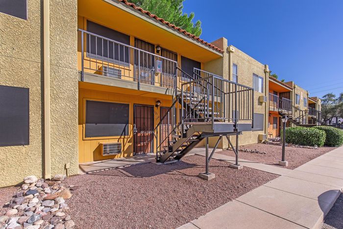 Charming two-story apartment building with vibrant yellow exterior, featuring modern metal railings and inviting outdoor stairs, set against a clear blue sky.