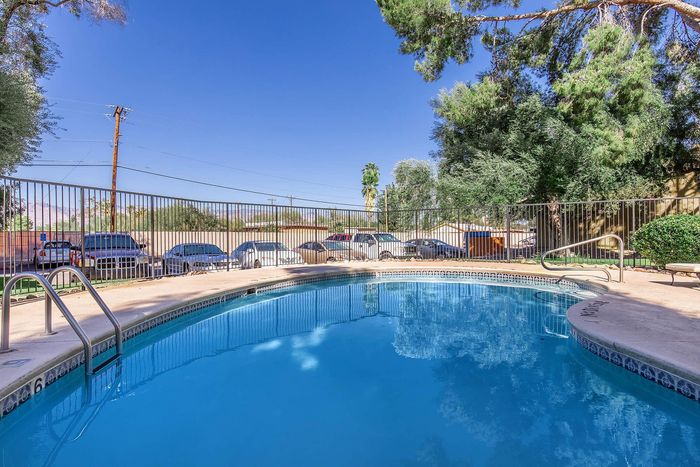 Inviting outdoor pool area with crystal clear water, surrounded by lush trees and a secure fence, perfect for relaxation and enjoyment.