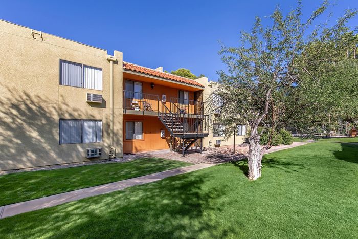 Charming apartment complex with a sunny balcony, lush green lawn, and vibrant trees, perfect for relaxing outdoors.