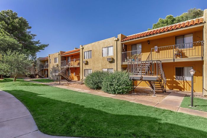 Charming apartment complex with vibrant orange and beige exteriors, lush green lawns, and inviting pathways under a clear blue sky.