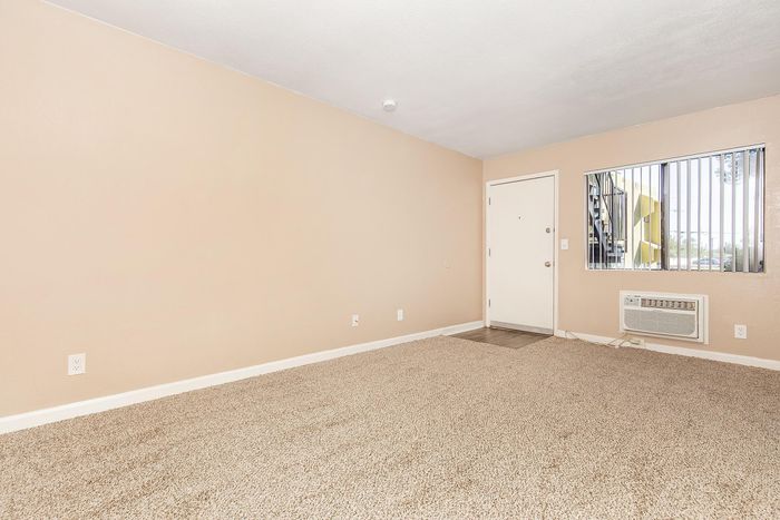 Bright and airy living space featuring plush carpet, modern air conditioning unit, and stylish beige walls.