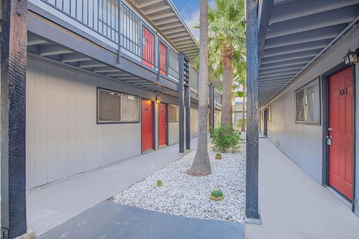 Charming apartment entryway with vibrant red doors and elegant landscaping featuring palm trees and cactus plants.