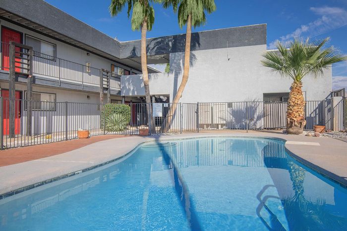Inviting modern apartment complex featuring a sparkling blue swimming pool surrounded by tropical palm trees under a clear sky.